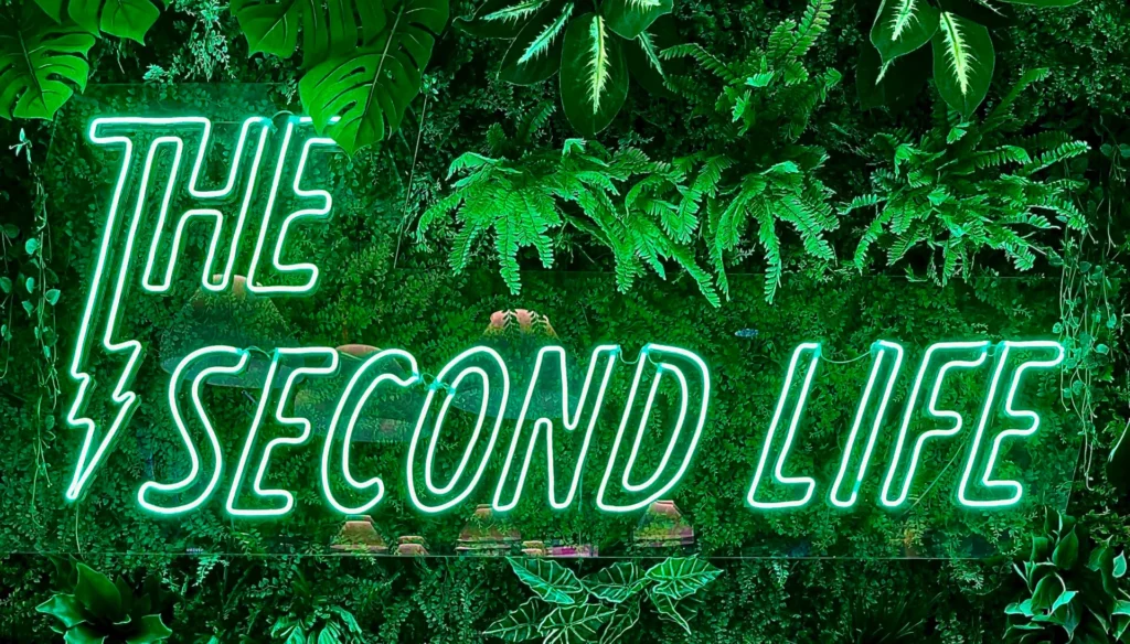 Enseigne néon "The Second Life" entourée de plantes vertes sur un mur végétal