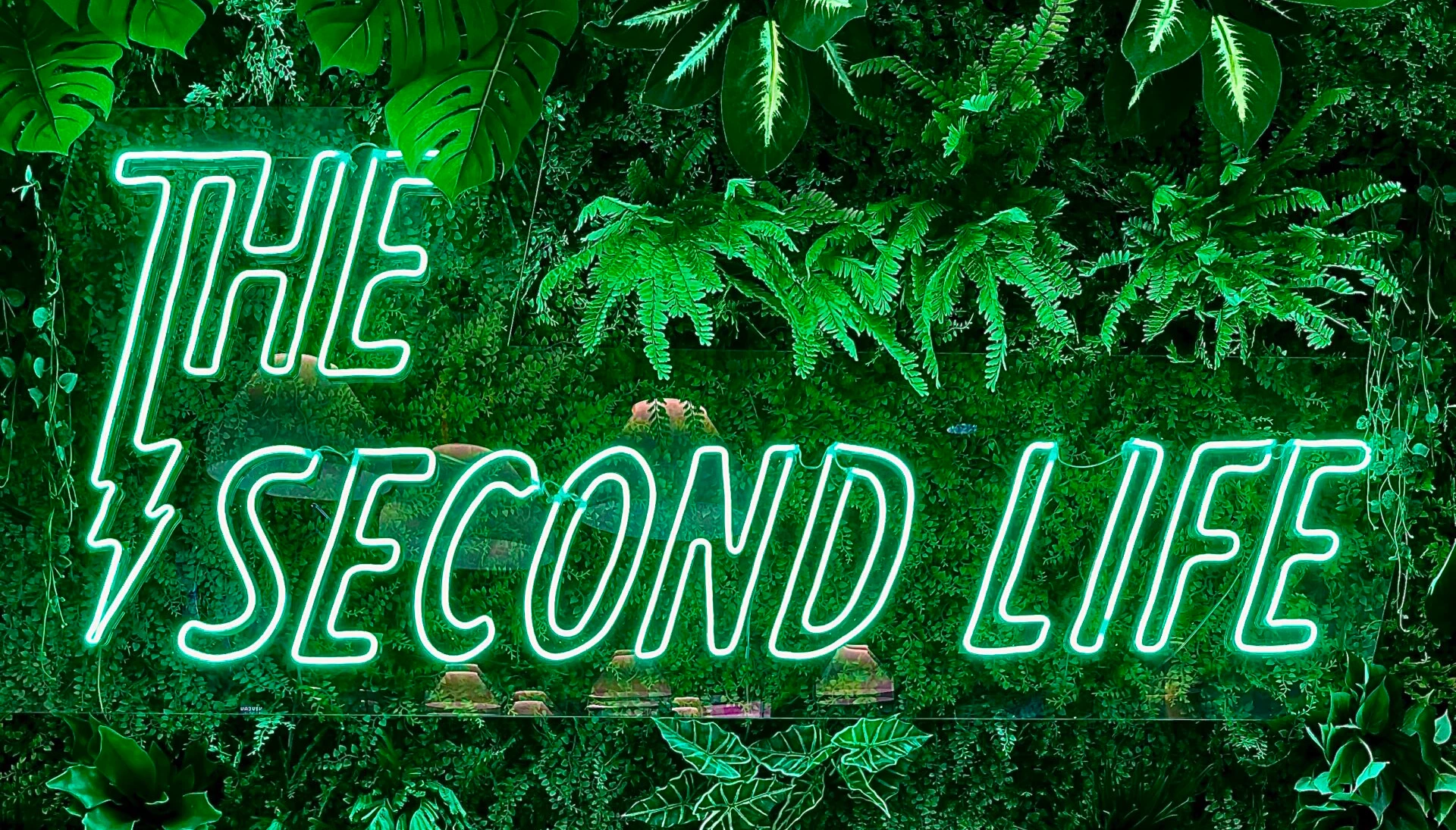 Le logo lumineux de The Second Life sur fond végétal, symbole d’un engagement éco-responsable.